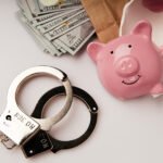 envelope with dollars, broken piggy bank and handcuffs on a tabl