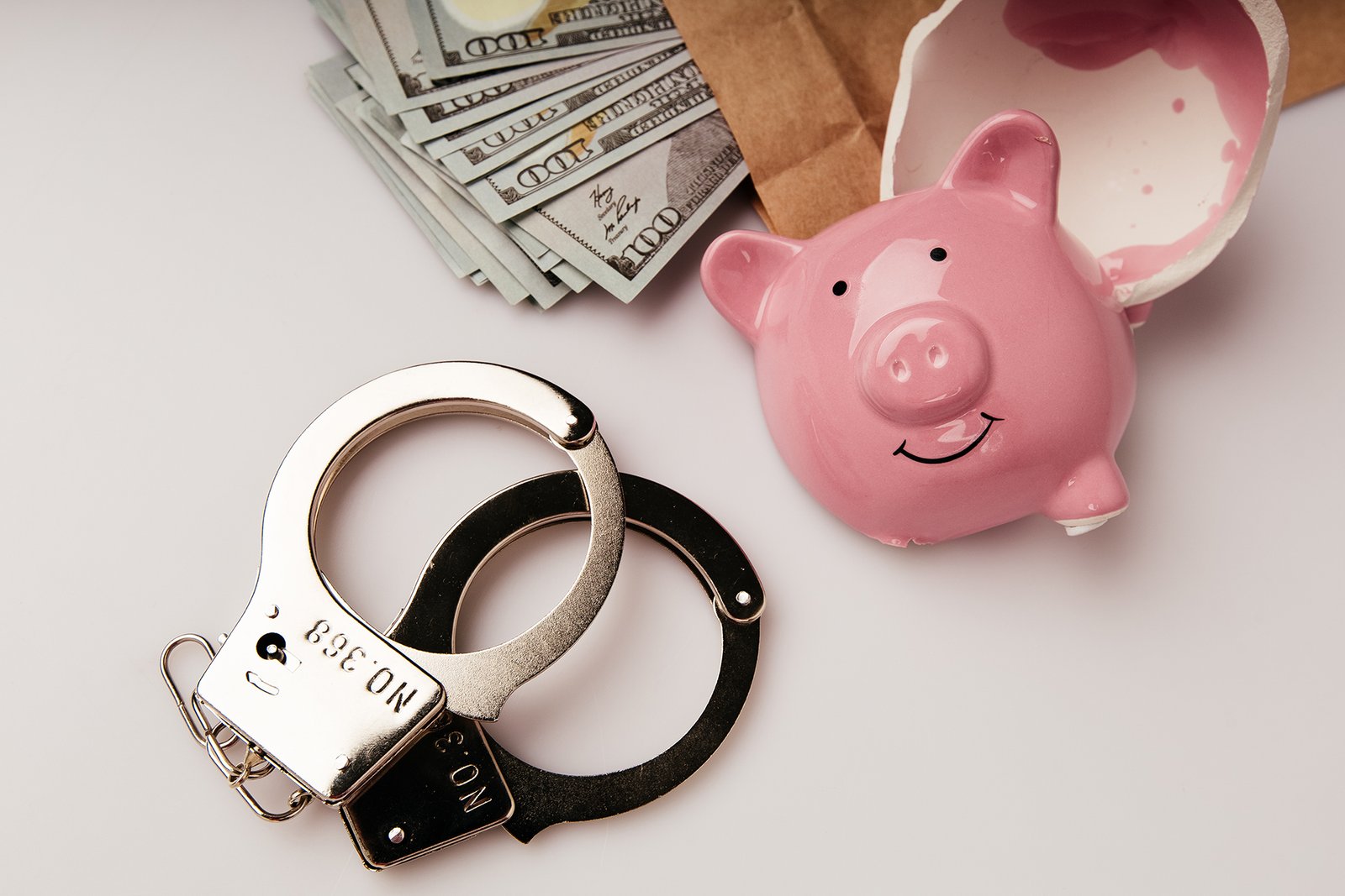 envelope with dollars, broken piggy bank and handcuffs on a tabl