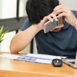 asian man stressed while calculate the credit card debt with a calculator and working on laptop at home, sad and dramatic, debt stress and mental health concept